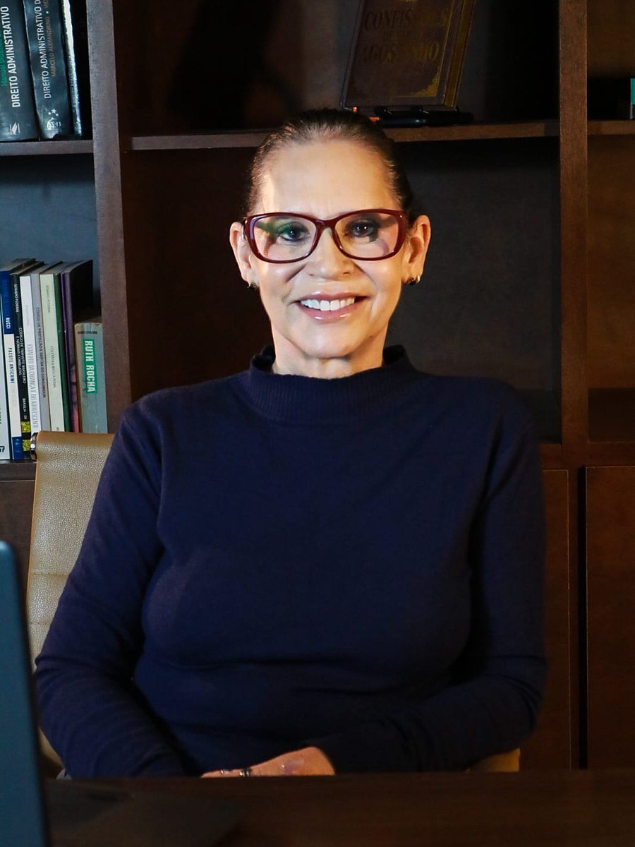 Andréia Braga sorrindo, sentada em frente a uma estante de livros